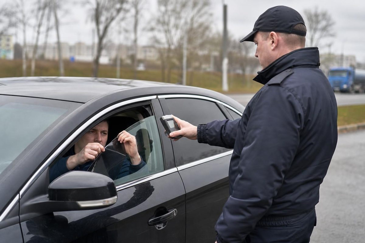Водитель снимает тёмную плёнку с переднего стекла под контролем дорожного инспектора